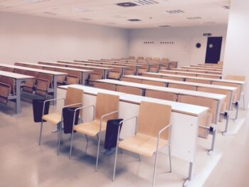 Aula de universidad con mesas colectivas y sillas con pala